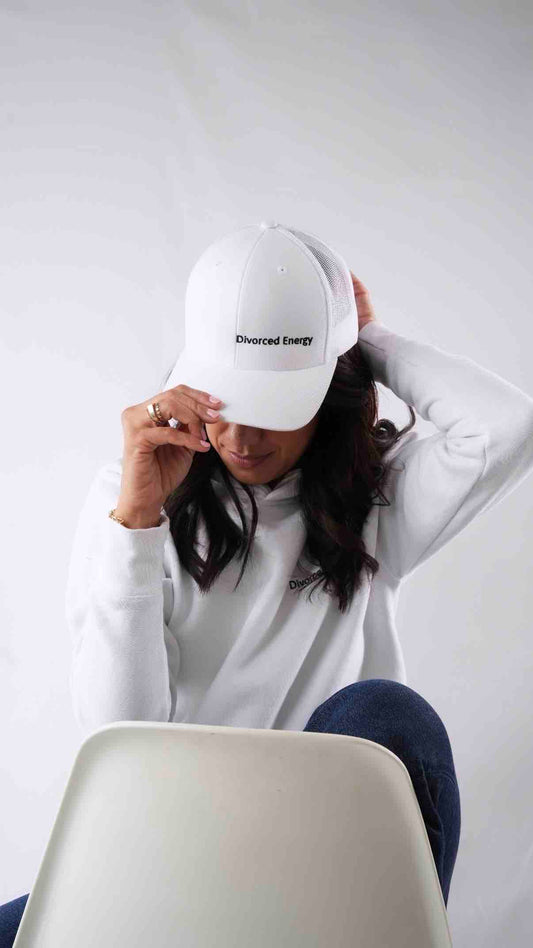 Person wearing a white cap and sweatshirt with text, sitting on a chair against a plain background