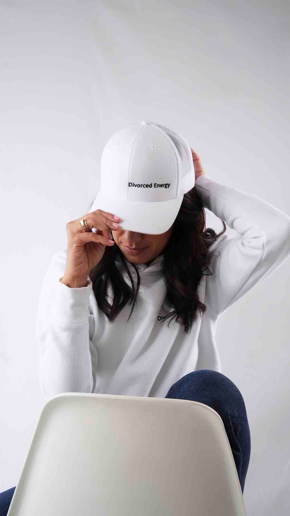 Person wearing a white cap and sweatshirt with text, sitting on a chair against a plain background